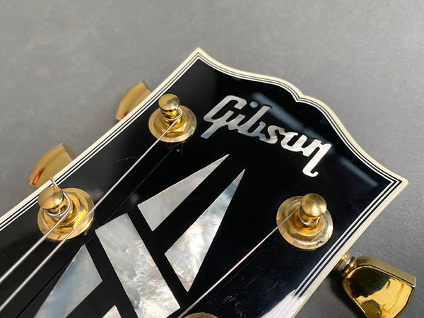 Close-up of Gibson guitar black headstock with mother-of-pearl inlay and gold tuning pegs on gray background
