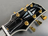 Close-up of Gibson guitar headstock with gold tuning pegs and mother-of-pearl inlay on black finish