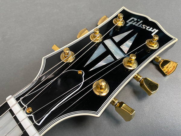 Close-up of Gibson guitar headstock with gold tuning pegs and mother-of-pearl inlay on black finish