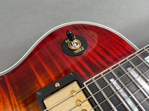 Close-up of electric guitar pickup selector switch set to treble on sunburst flame maple top with black and gold hardware and pearl inlay fretboard