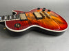 Electric guitar with sunburst flame maple top, gold hardware, black control knobs, and white binding on gray surface