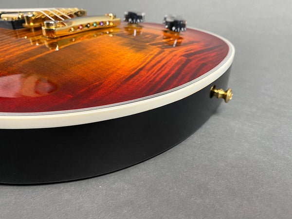 Close-up of sunburst electric guitar body with gold hardware and cream binding on gray background
