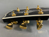 Close-up of black guitar headstock with gold tuning pegs and white binding on gray background