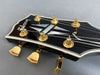 Close-up of Gibson guitar headstock with gold tuning pegs and mother-of-pearl inlay on black finish