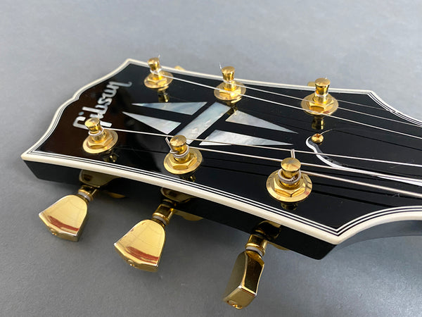 Close-up of Gibson guitar headstock with gold tuning pegs and mother-of-pearl inlay on black finish