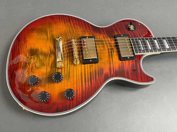 Electric guitar with sunburst finish, dual humbucker pickups, four black control knobs, gold hardware, and cream binding on the body and neck.