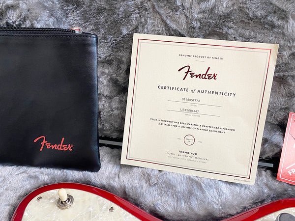 Fender certificate of authenticity with black Fender pouch and red guitar body on gray plush background