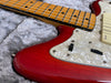 Close-up of red electric guitar body with white pearloid pickguard and maple fretboard on gray plush background