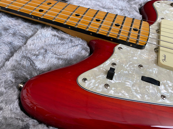 Close-up of red electric guitar body with white pearloid pickguard and maple fretboard on gray plush background