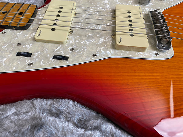 Close-up of Fender Jazzmaster guitar pickups and pearl white pickguard on sunburst wooden body with metal bridge and strings on plush gray surface