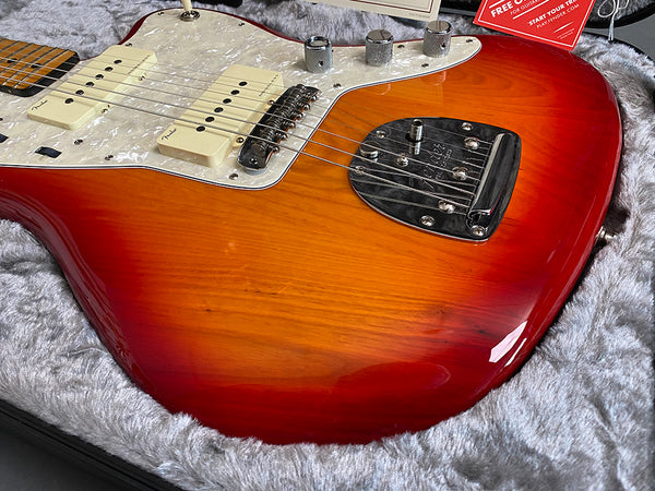 Close-up of sunburst Fender electric guitar body with pearl white pickguard, chrome bridge, and control knobs resting in a soft gray guitar case lining