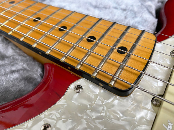 Close-up of red electric guitar maple fretboard with metal frets and pearl white pickguard on gray fabric background