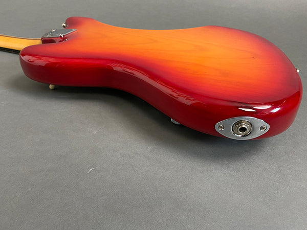 Close-up view of the back side of a red sunburst electric guitar body with a glossy finish and input jack on a gray background.