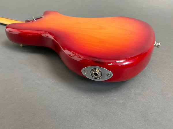 Back close-up view of red sunburst electric guitar body with silver output jack plate on gray surface