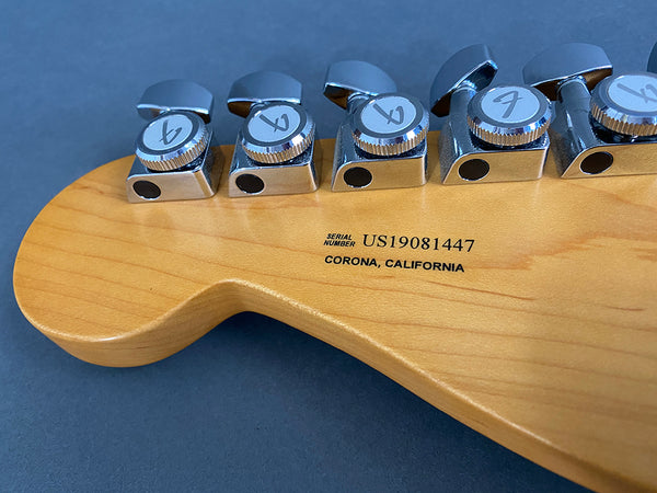 Close-up of guitar headstock showing six chrome tuning pegs and serial number US19081447 with Corona, California printed on maple wood surface
