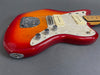 Close-up of red sunburst jazzmaster electric guitar body with white pearl pickguard and chrome control knobs on gray background