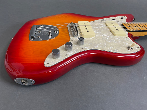 Close-up of red sunburst jazzmaster electric guitar body with white pearl pickguard and chrome control knobs on gray background