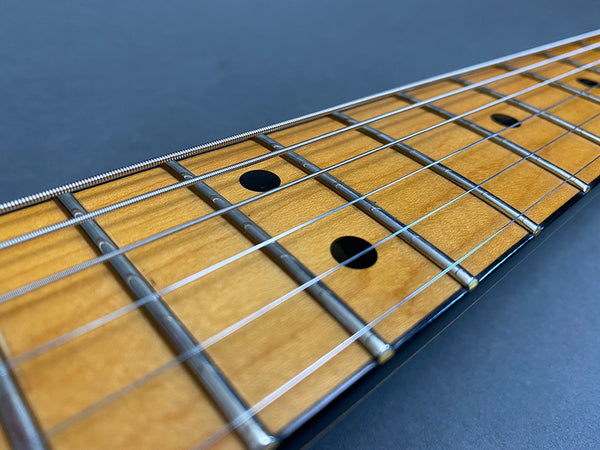 Close-up of guitar maple fretboard with metal frets and steel strings on dark background
