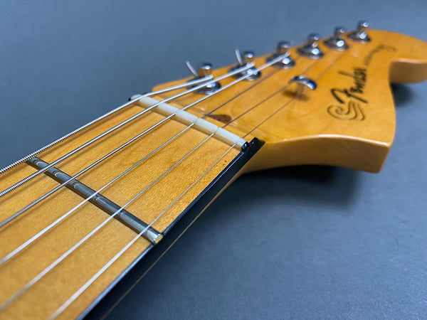Close-up of Fender Stratocaster electric guitar headstock with strings and tuning pegs on gray background