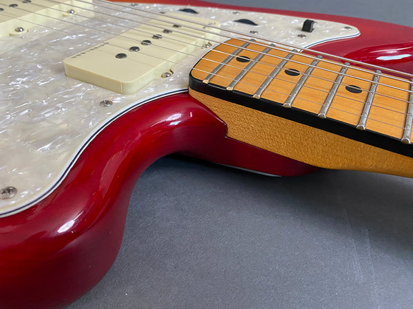 Close-up of red electric guitar body with cream pickup, pearl white pickguard, and maple neck showing frets and strings