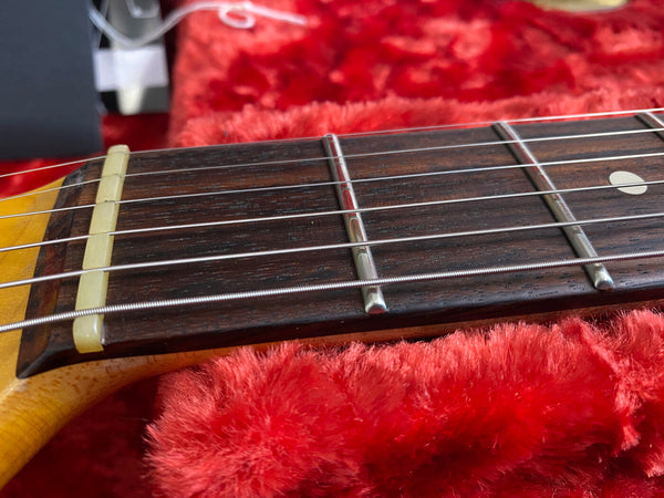 Close-up of vintage guitar neck and fretboard with metal frets and nylon strings on red plush case lining