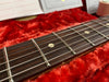 Close-up of guitar fretboard with metal frets and dot inlays on dark wood against red plush guitar case lining