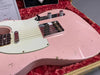 Close-up of pink vintage Fender Telecaster electric guitar body with white pickguard, chrome bridge and control knobs, showing wear and aging in a red plush-lined tweed case with Fender certificate visible in background