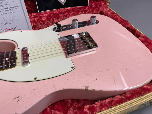 Close-up of pink vintage Fender Telecaster electric guitar body with white pickguard, chrome bridge and control knobs, showing wear and aging in a red plush-lined tweed case with Fender certificate visible in background