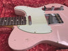 Close-up of vintage pink electric guitar body with white pickguard, chrome bridge, and control knobs on red velvet background