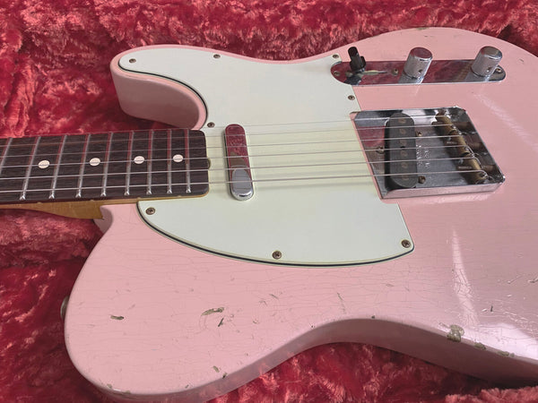 Close-up of vintage pink electric guitar body with white pickguard, chrome bridge, and control knobs on red velvet background