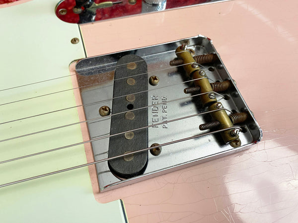 Close-up of vintage Fender guitar bridge and pickup with metal plate and strings on a light pink body with aging cracks