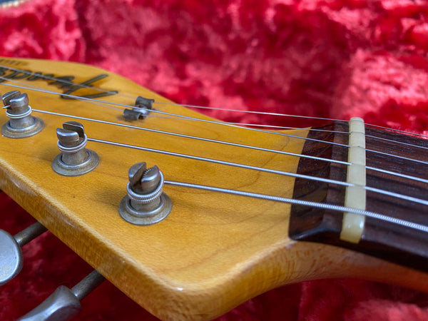 Close-up of vintage electric guitar headstock with tuning pegs, metal strings, and nut on wood fretboard, resting on red plush fabric background