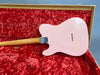 Back of pink Gibson guitar body with maple neck and chrome neck plate inside vintage red plush-lined tweed guitar case