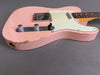 Close-up of pink electric guitar body with chrome control knobs and white pickguard, showing worn and distressed finish details, on gray background.