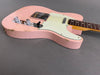 Close-up of a vintage pink electric guitar body with white pickguard, chrome control knobs, and visible wear and scratches on a gray background.