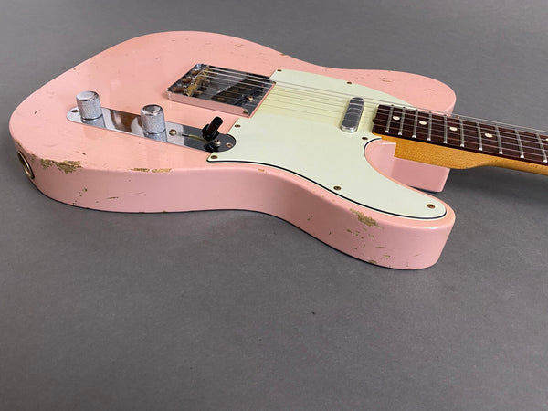 Close-up of a vintage pink electric guitar body with white pickguard, chrome control knobs, and visible wear and scratches on a gray background.