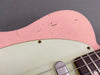 Close-up of pink electric guitar body with vintage crackle finish and white pickguard showing metal screw and part of the rosewood fretboard with strings.