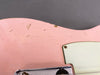 Close-up of vintage pink electric guitar body showing cracked paint and aging wear near white pickguard and metal bridge plate