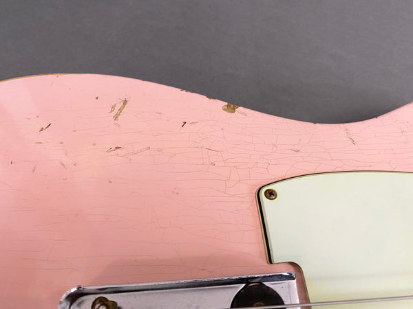 Close-up of vintage pink electric guitar body showing cracked paint and aging wear near white pickguard and metal bridge plate