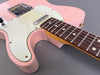 Close-up of pink electric guitar body with cream pickguard and rosewood fingerboard on gray background, showing vintage wear and metal bridge.