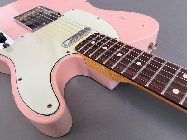 Close-up of pink electric guitar body with cream pickguard and rosewood fingerboard on gray background, showing vintage wear and metal bridge.