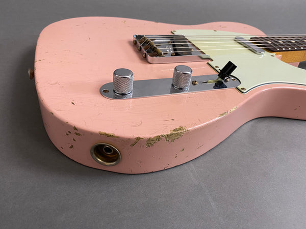 Close-up of pink electric guitar body with vintage wear, chrome control knobs, and white pickguard on gray background