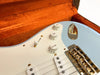 Close-up of light blue electric guitar body with white pickguard, white tone and volume knobs, and gold hardware in an orange plush guitar case interior.