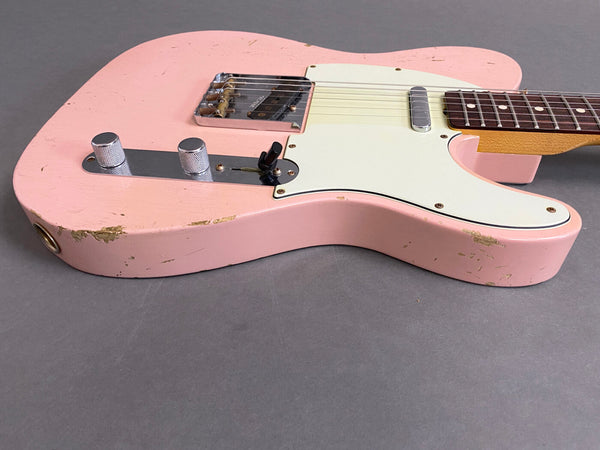 Close-up of pink electric guitar body with white pickguard and two chrome control knobs showing vintage wear and paint chips on gray background
