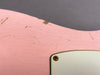Close-up of pink electric guitar body showing vintage-style paint cracks and aging with screw detail on white backplate