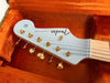 Close-up of Fender Stratocaster electric guitar headstock with gold tuning pegs inside orange plush-lined guitar case