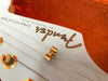 Close-up of white Fender Stratocaster guitar headstock with gold tuning pegs and strings against orange background