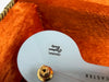 Close-up of white guitar body inside orange plush-lined case showing "Original Contour Body" sticker near gold strap button