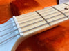 Close-up of guitar neck and strings with light wood fretboard and white nut on an orange plush background