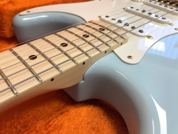 Close-up of light blue electric guitar neck and body with maple fretboard and metal strings on orange fabric background